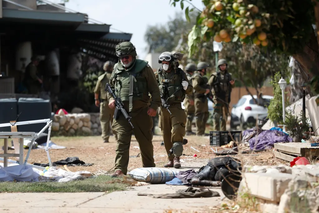 Soldados israelenses caminham ao lado do corpo de um militante do Hamas morto no kibutz Kfar Aza, próximo à fronteira com Gaza, em 10 de outubro de 2023 / ATEF SAFADI/EPA-EFE/Shutterstock